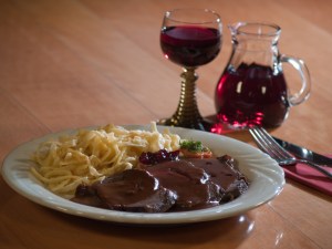 Braten mit Spätzle und ein Glas Rotwein auf dem Holztisch