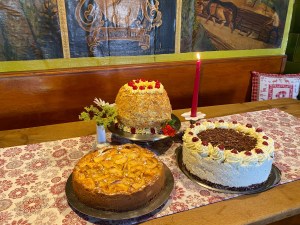 Hausgemachte Torten und Kuchen auf einem Tisch in der Gaststube, vor bemalten Wandtafeln