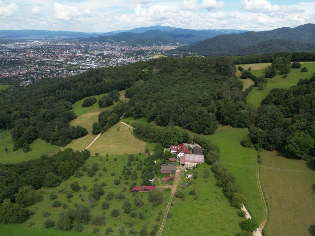 Der Schönberghof zwischen Streuobstwiesen und Wald, dahinter Freiburg und der Schwarzwald, Luftaufnahme