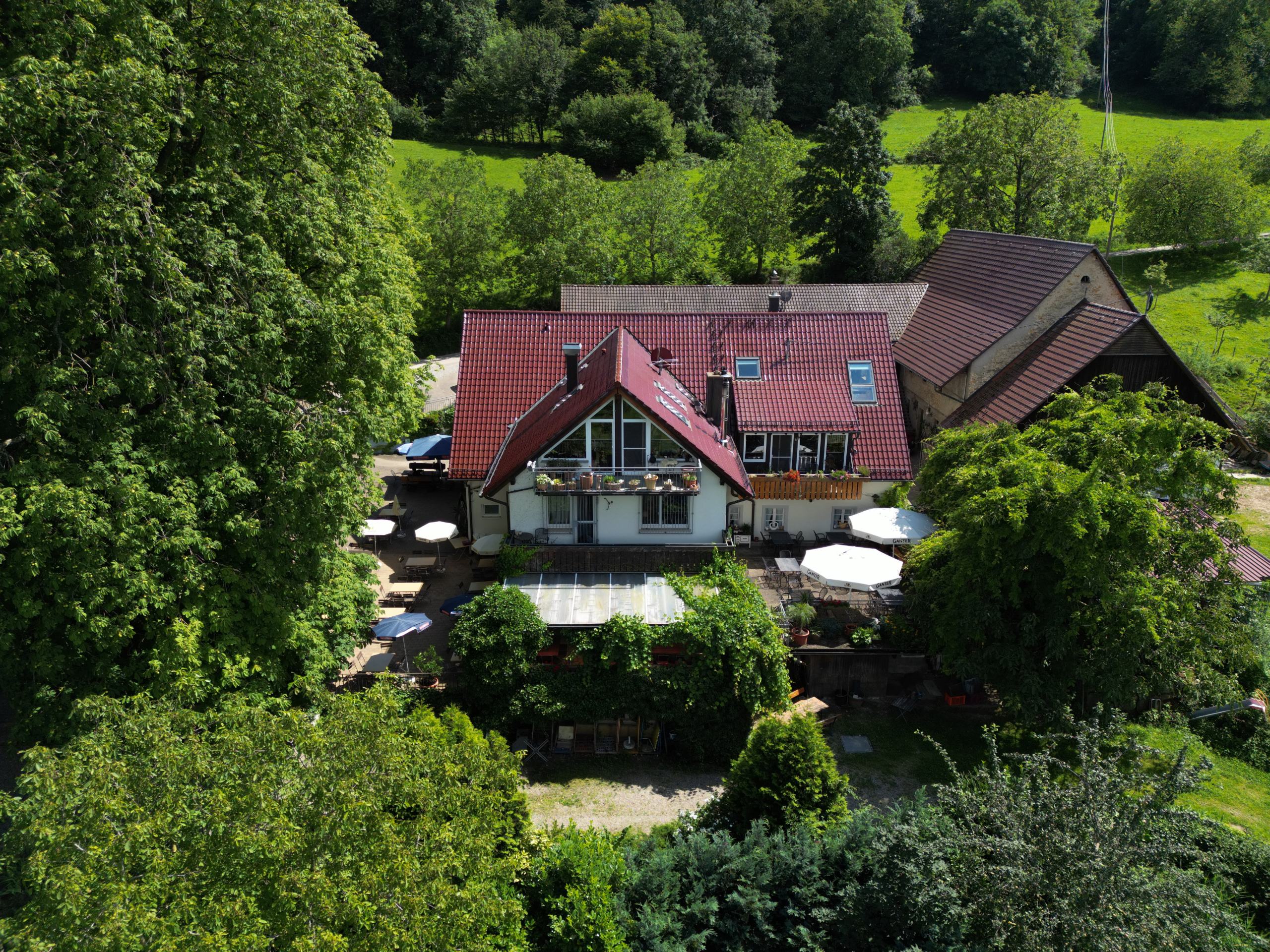 Das Gasthaus Schönberghof mit Terrasse und Sonnenschirmen, Luftaufnahme von vorn