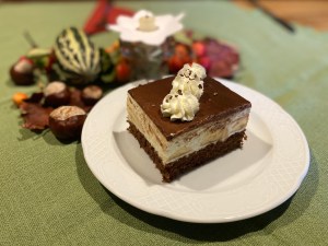 Ein Stück Torte mit Sahnetupfen, daneben Herbstdeko mit Kastanien und Zierkürbis