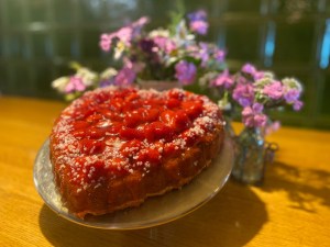 Erdbeerkuchen in Herzform mit Hagelzucker, dahinter Sommerblumen